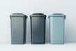 © Nopadol - Three Recycling Bins: Three sleek, modern recycling bins in dark gray, charcoal, and light teal stand in a row against a simple backdrop.