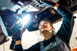© unai - Female mechanic inspecting car chassis with flashlight in workshop