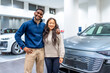 © unai - Happy multiethnic couple buying electric car at dealership showroom