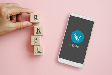 BNPL, buy now pay later, on wooden cube blocks and white mobile phone with shopping cart icon on pink background