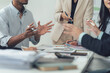 © Kritdanai - Business Team Brainstorming: A diverse group of professionals actively engaged in a collaborative meeting, sharing ideas and strategies around a table filled with documents and office supplies.