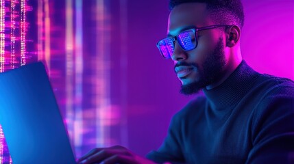 a man with a beard wearing glasses types on a laptop. he is illuminated by purple and blue neon ligh