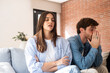 © simona - Young adult couple sitting apart on a sofa at home, having a serious discussion after trust was broken due to infidelity, experiencing emotional distance, tension, and considering separation
