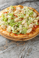 Wall Mural - Caesar pizza with white sauce, cheese, tomatoes, chicken breast and lettuce close-up on a wooden board on the table. Vertical