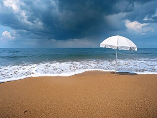 Wall Mural - Beach summer marketing campaigns concept. A solitary white umbrella stands on a sandy beach under a dramatic sky, with waves gently lapping at the shore.