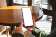 © Farknot Architect - Mockup image of a woman holding mobile phone with blank desktop screen in cafe