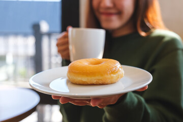 Poster - Closeup of a young woman holding and drinking hot coffee and eating donut in cafe