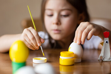 child paints eggs for Easter at home at table. kids craft - egg stand made from packaging carton