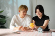 © itchaznong - Young couple collaborating on real estate planning while analyzing a miniature home and budget