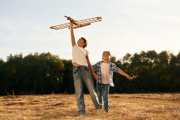 Having fun. Boy and girl are playing with wooden toy plane on the field