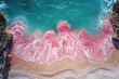 © artdolgov - A breathtaking aerial perspective reveals vibrant pink waves gently crashing onto a soft sandy beach. The contrast of colors creates a serene and picturesque coastal landscape.