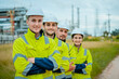 © Hip.hub - Four construction workers pose confidently at a power plant site during daylight, showcasing teamwork and safety gear