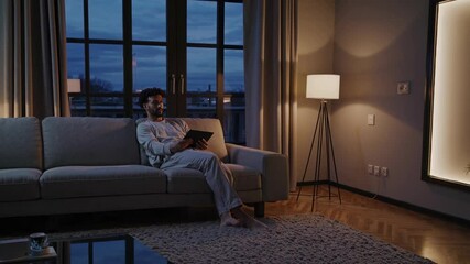 Poster - Man relaxing in a futuristic living room with ambient lighting and VFX hologram effects at dusk