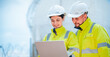 © Hip.hub - Engineers collaborate on a laptop at a construction site in daylight with safety gear and focused expressions