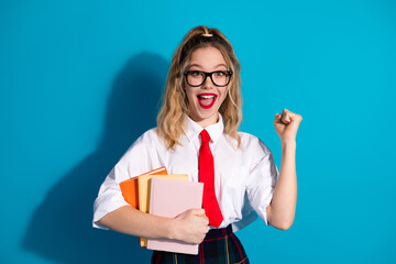 Excited young woman in stylish uniform holding books against vibrant blue background, expressing joy and enthusiasm