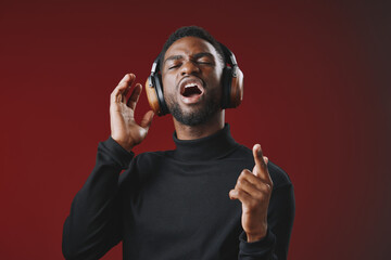 A joyful Black man singing while wearing headphones against a vibrant red background, expressing passion and enjoyment for music, ideal for music and lifestyle themes