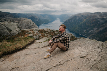 Wall Mural - Man Sitting on Cliff Overlooking Fjord