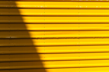  Bright sunlight casting a diagonal shadow on a vivid yellow corrugated metal wall, creating an interesting abstract pattern of light and shade