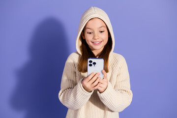 Wall Mural - Smiling young girl in a casual hoodie interacting with a smartphone on a purple background