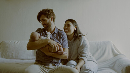 Wall Mural - Mom, dad and baby on a sofa in the living room of their home together for love, care or bonding. Family, smile and relax with happy young parents holding their cute newborn infant chid in a house