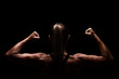 © Nikola Spasenoski - Rear view of a muscular woman flexing arms in a dramatic dark environment symbolizing strength and dedication