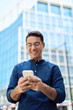 © insta_photos - Happy professional businessman holding smartphone in hands looking at cellphone outdoor, young Hispanic business man customer using finance banking mobile app on cell phone standing in city. Vertical.