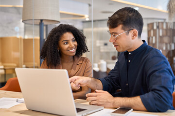 Aufkleber - Two young busy diverse coworkers business people using laptop at office meeting. Smiling team professional colleagues working together on computer discussing online technology data at work desk.