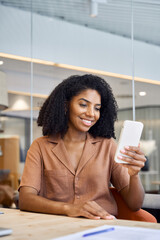Aufkleber - Professional female employee or entrepreneur looking at smartphone working with cellphone in hands. Young happy African American business woman using mobile phone sitting in corporate office. Vertical