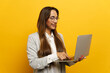 © muse studio - Woman in a gray cardigan smiles while using a laptop against a vibrant yellow background