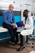 © DC Studio - Friendly black doctor holds clipboard to carefully explain healthcare treatment to retired white man in hospital room. Caucasian old patient having medical discussion with african american physician.
