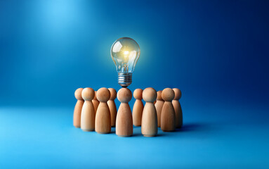 Leinwandbilder - A glowing light bulb shines above a circle of wooden figures.