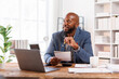 © David - An office scene showing a professional at his desk, using a laptop for various business activities and strategies.African American Businessman work.