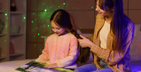 Poster - Young mother doing her little daughter's hair with book in bedroom at night