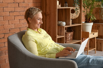 Wall Mural - Mature female freelancer working with laptop in armchair at home