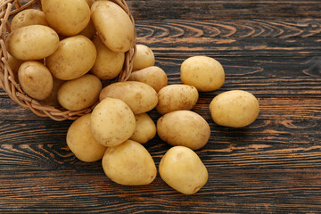 Wall Mural - Wicker bowl with raw potatoes on wooden background