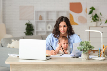 Canvas Print - Cute little baby and young mother working with laptop while writing in notebook on maternity leave at home