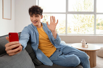 Wall Mural - Young man video chatting with mobile phone on sofa at home