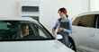 © m-art - A woman in formal clothes chooses a car at a car dealership. She sits in the driver's seat. The manager is talking to her standing nearby