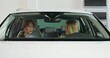© m-art - A car dealership manager and a stylish female customer are sitting in a car. They're talking, looking around. Front view