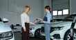 © m-art - The manager hands over the car keys to the buyer. They shake hands and smile. A stylish woman bought a car at a car dealership