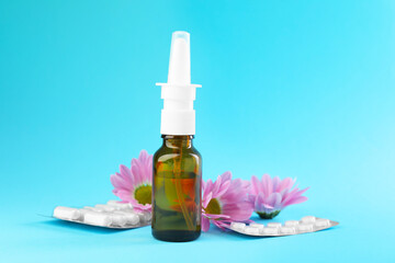 Wall Mural - Allergy treatment. Nasal spray, pills and flowers on light blue background