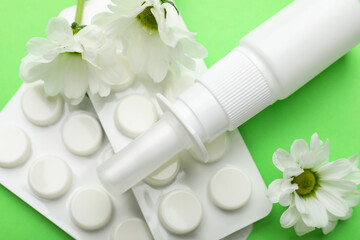 Wall Mural - Allergy treatment. Nasal spray, pills and flowers on green background, closeup