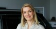 © m-art - A stylish woman smiles looking at the camera standing next to a car in a car dealership