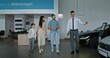 © m-art - The car dealership manager shows cars to customers by taking them through the showroom. A family with a child chooses a car