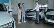 © m-art - The car dealership manager hands over the keys of the new car to customers and shakes their hands while standing in the showroom