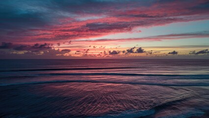 Poster - Vibrant twilight sunset over the sea with deep pink and orange hues reflected on gentle waves creating a serene coastal landscape