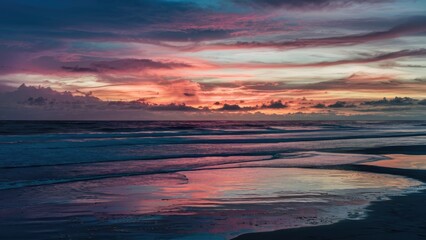 Aufkleber - Vibrant twilight sunset over calm ocean reflecting hues of pink, purple, and blue on wet sand creating a serene and picturesque landscape.