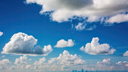 Poster - Vibrant blue sky filled with fluffy white clouds scattered across the horizon above a distant city skyline captured in a peaceful outdoor scene.