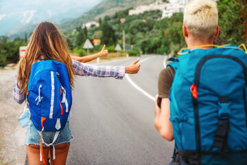 Wall Mural - cheerful interracial friends standing on road showing hitchhiking gestures. tourism traveling