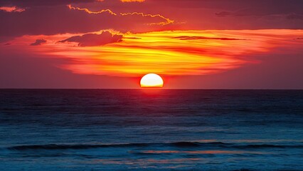 Poster - Vibrant orange sunset illuminating the ocean with deep blue hues on the horizon featuring soft clouds and gentle waves in the foreground
